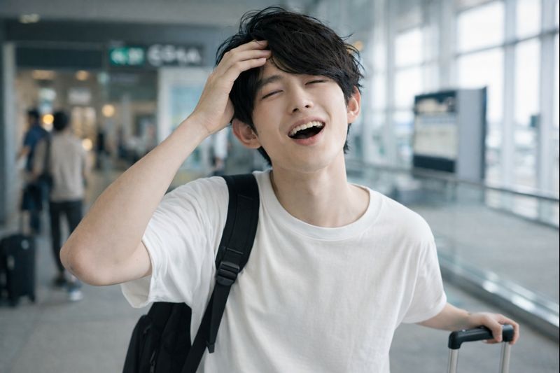 空港に到着し、スーツケースを引きながら少し慌てた表情を見せるアジア人男性
