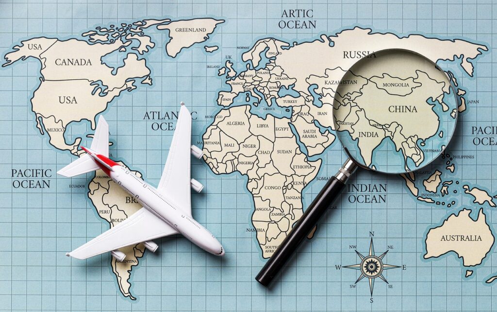 世界地図と飛行機、虫眼鏡で旅行先を探すイメージ画像